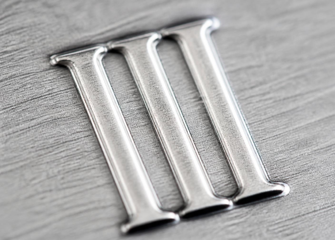 Macro detail of the embossed III monogram on brushed aluminium